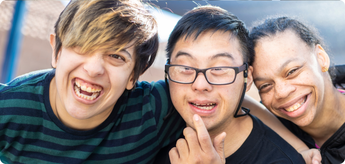 Three friends with disabilities smiling and embracing, showcasing friendship and inclusion.